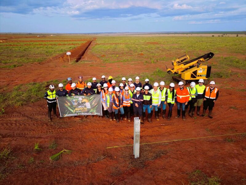 Team of professionals wearing safety equipment at an infrastructure construction site, gathered in a field area.