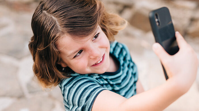 Child holding a smartphone in front of a social media screen, representing the court injunction against child labor on social media platforms without prior authorization.